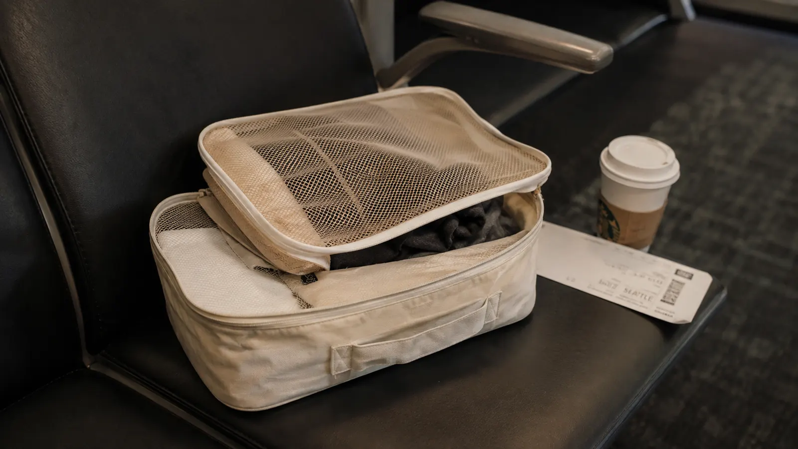 Worn cream BAGAIL packing cube with a slightly frayed mesh corner sitting open on an airport lounge chair