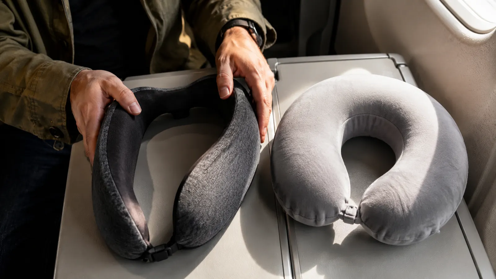 A memory foam neck pillow and a deflated inflatable travel pillow laid side by side on an airplane tray table
